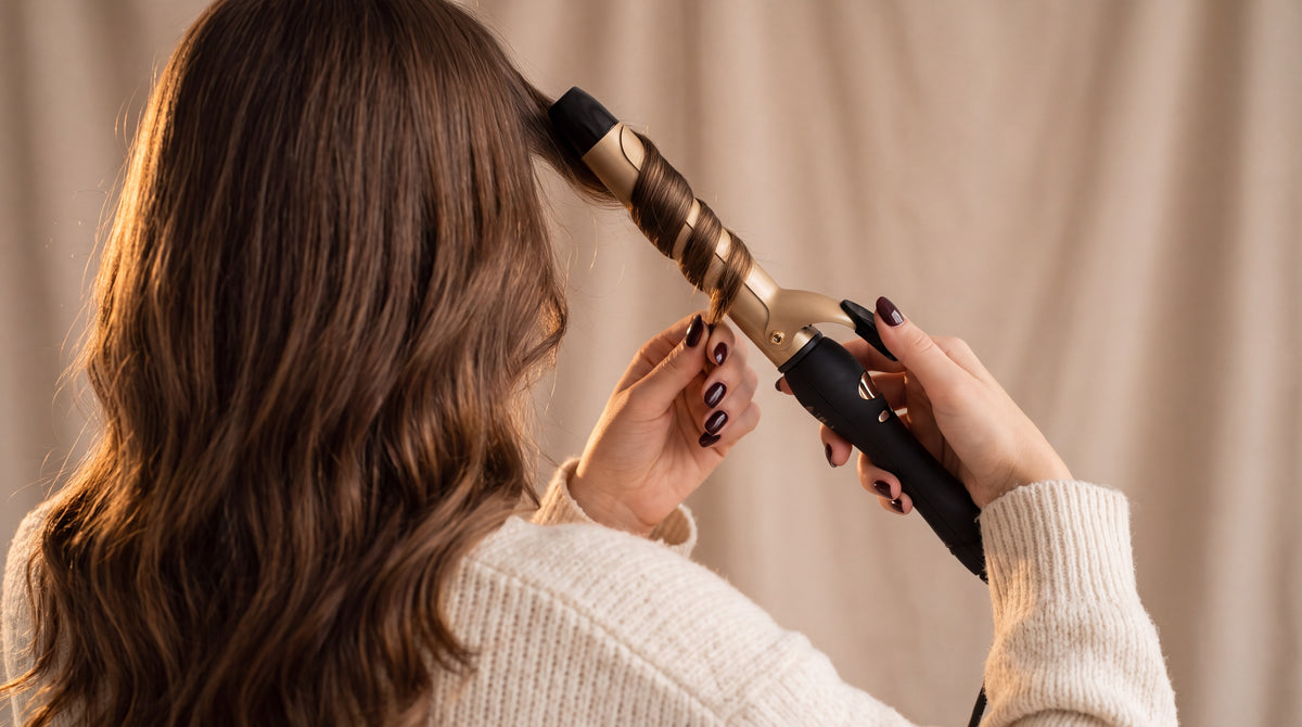 Mujer rizando su cabello castaño con un rizador cerámico negro y dorado, categoría Rizadores de BRILLABONITA™